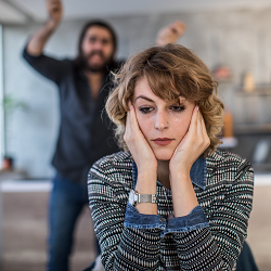A woman covers her ears as her partner appears to yell at her in the background. A marriage counselor in California can help you be assertive in your relationship. Search “marriage counseling near me” to learn how Roseville relationship counseling ca